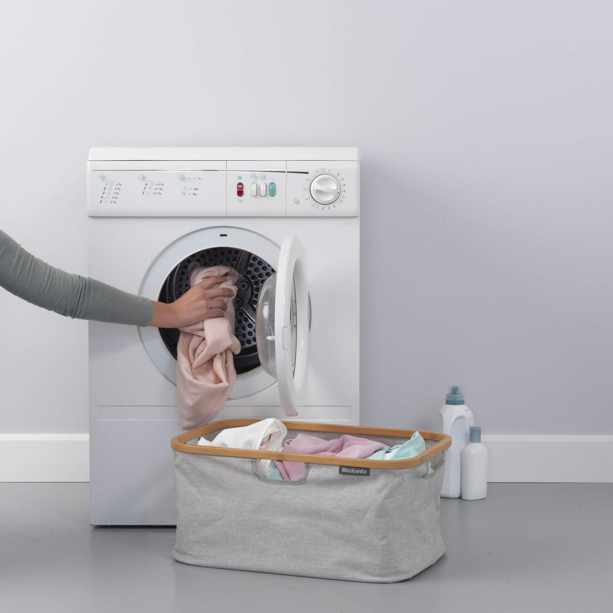 Laundry being placed into the machine from a bamboo and fabric foldable laundry basket