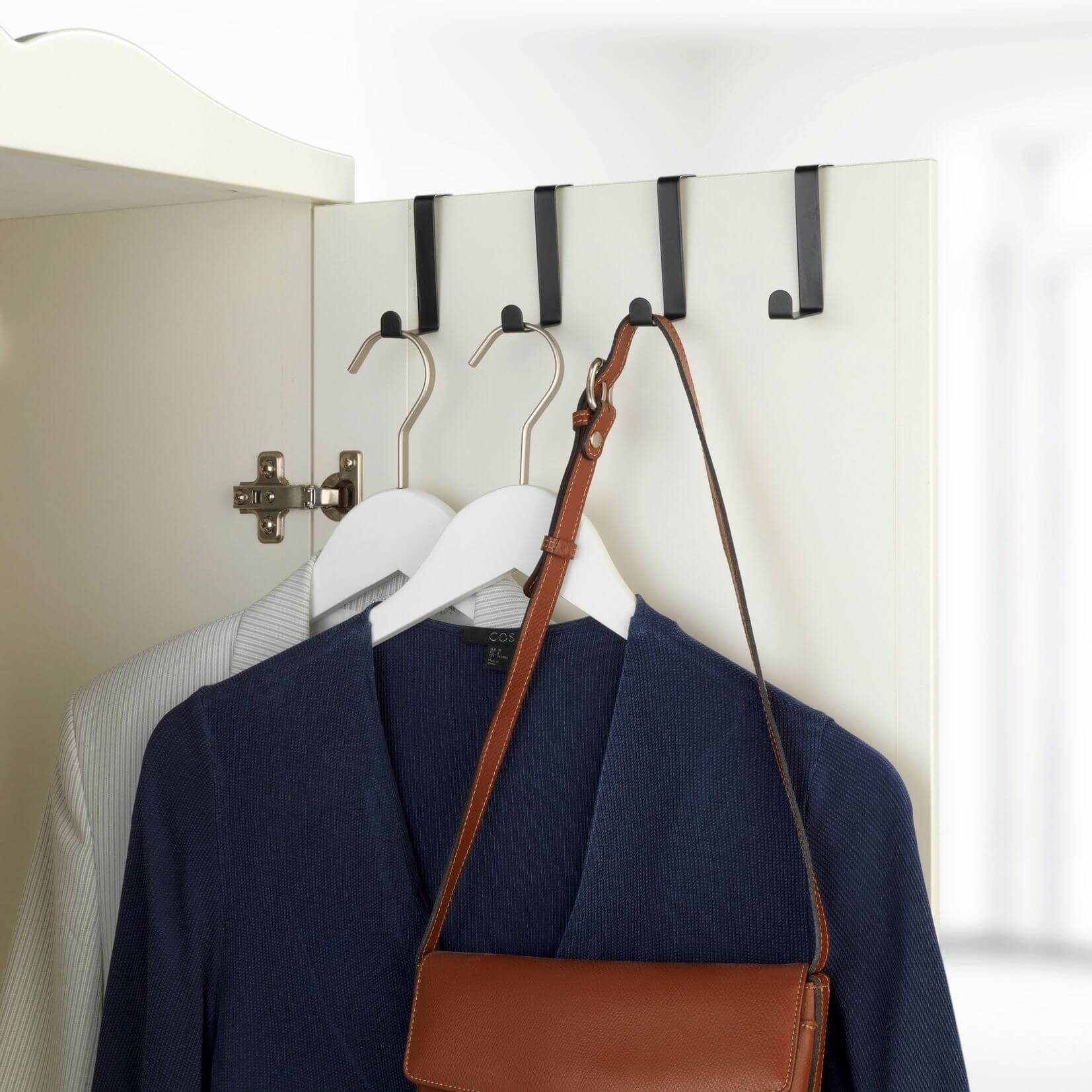 Four black over the door storage hooks holding a handbag and jumpers