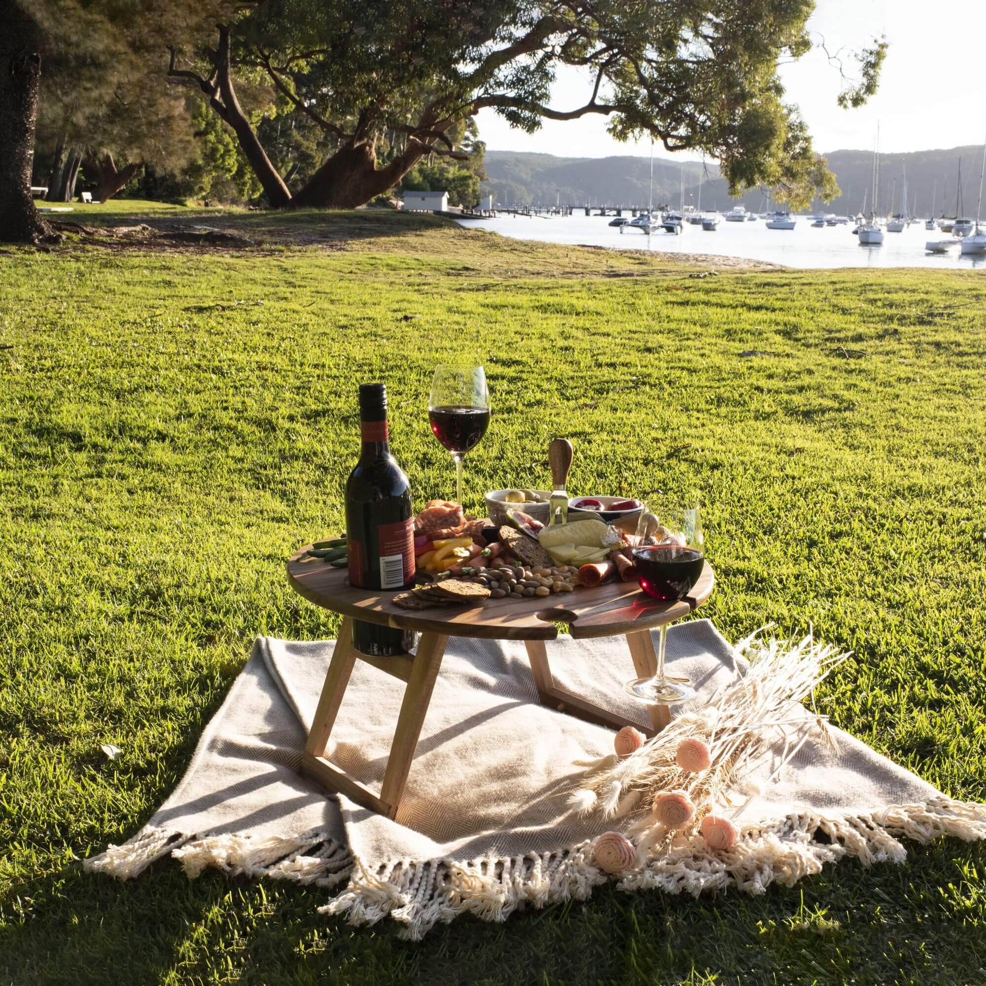 Round timber picnic table on a picnic rug by the sea