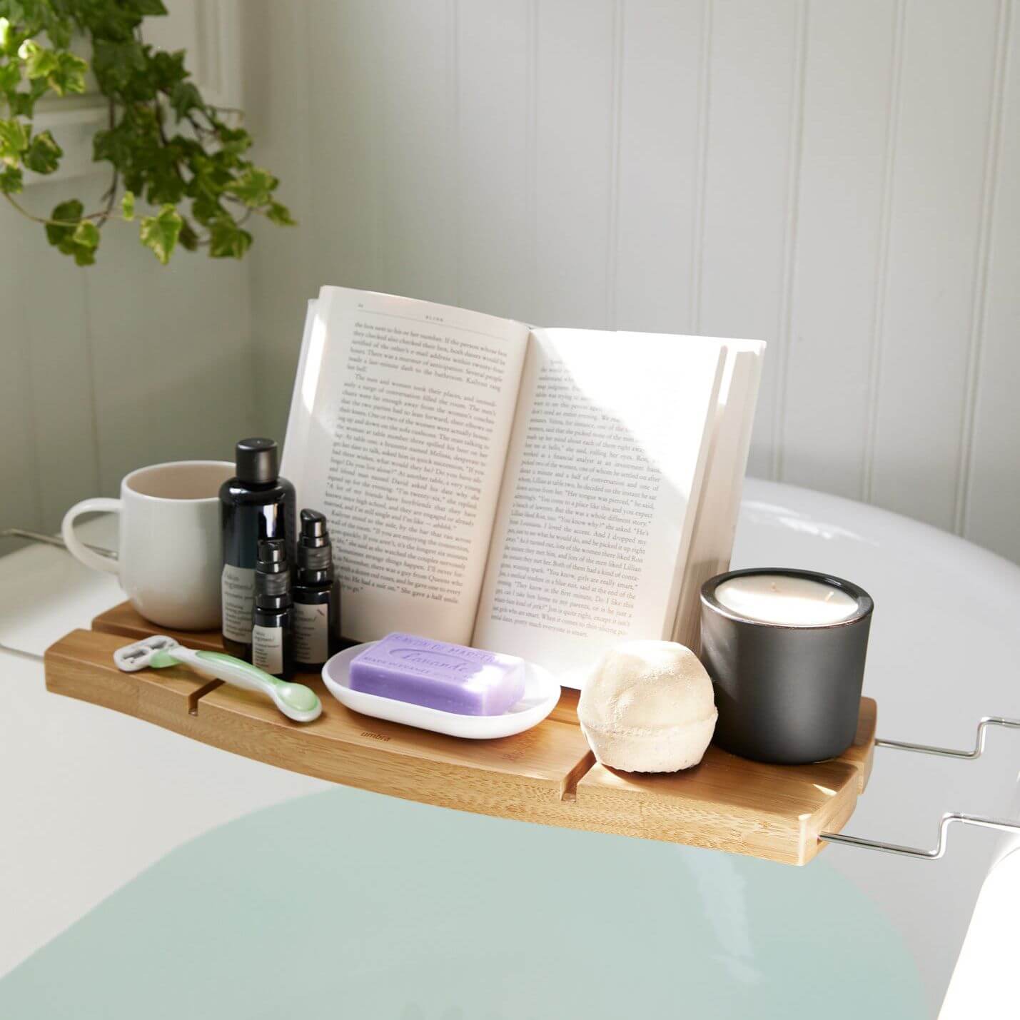 Bamboo bath caddy holding a book, candle and other bathroom accessories above a bathtub