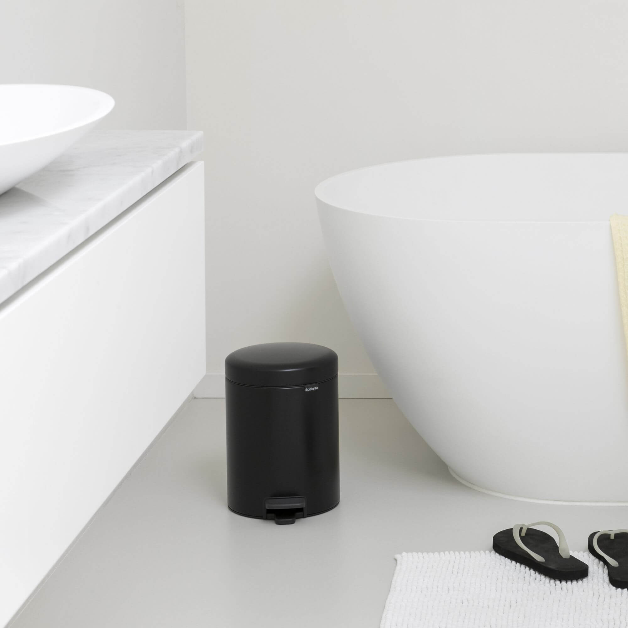 A matte black Brabantia rubbish bin in a modern, white bathroom