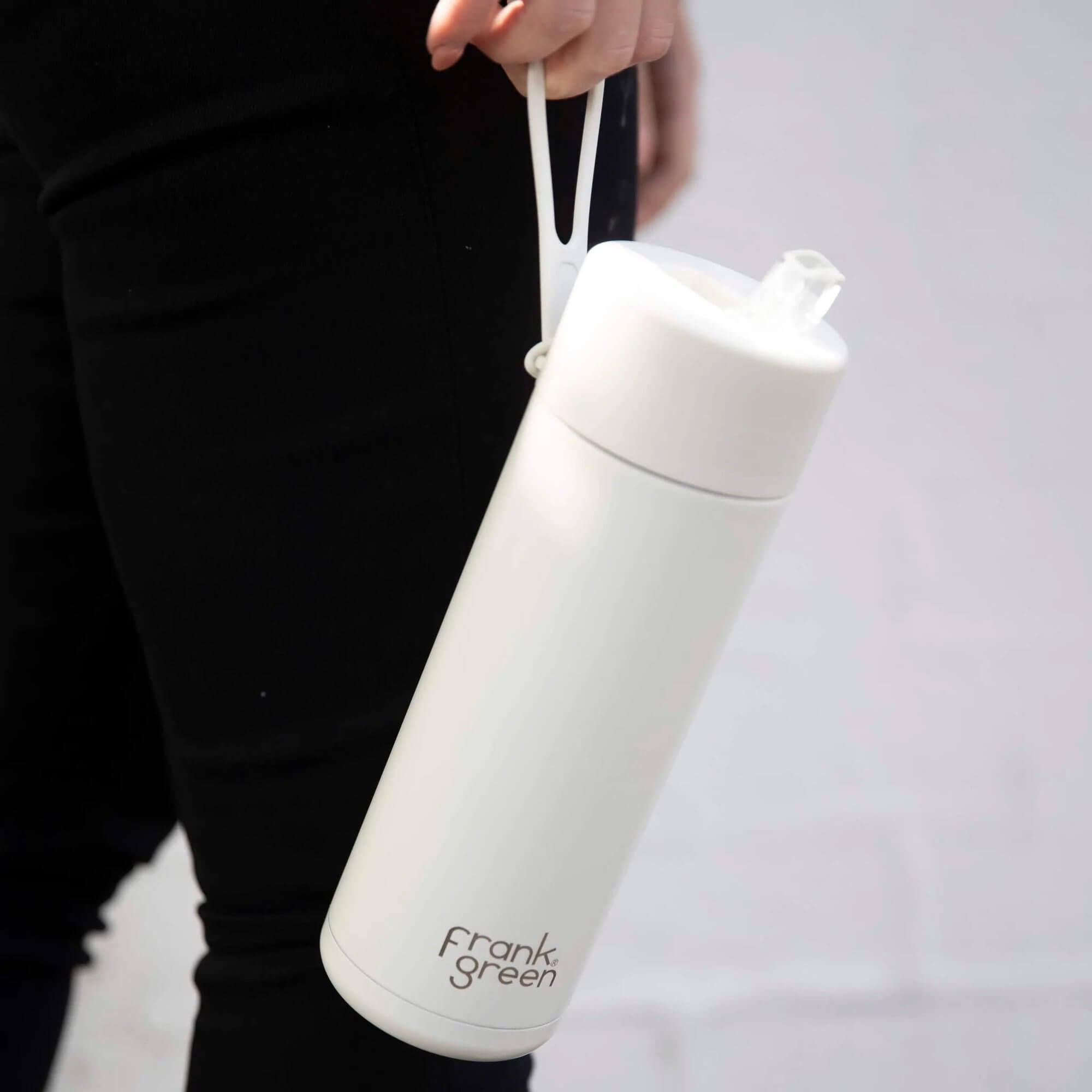 A Cloud White reusable water bottle from Frank Green being carried by the strap
