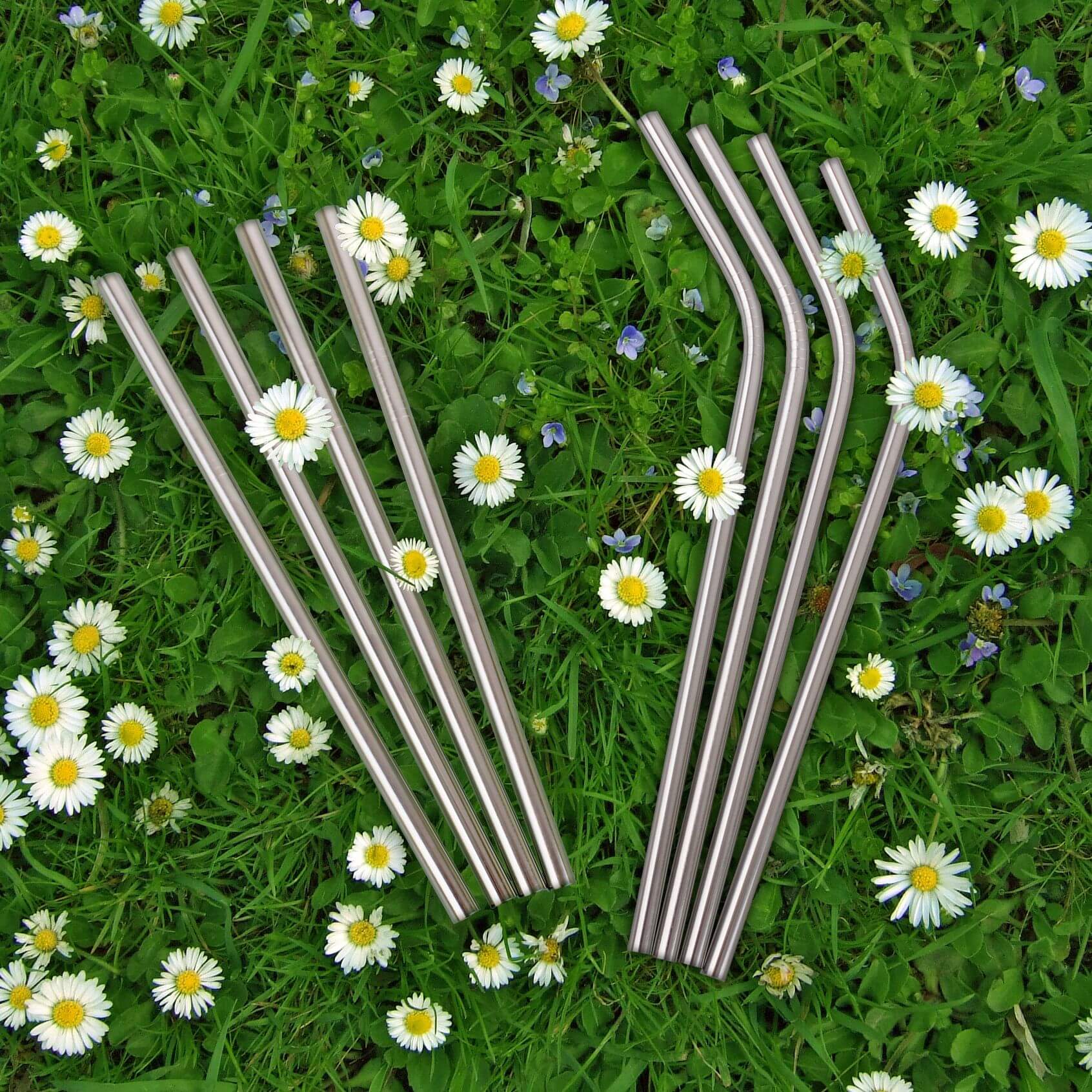 Stainless steel reusable straws on grass with yellow flowers