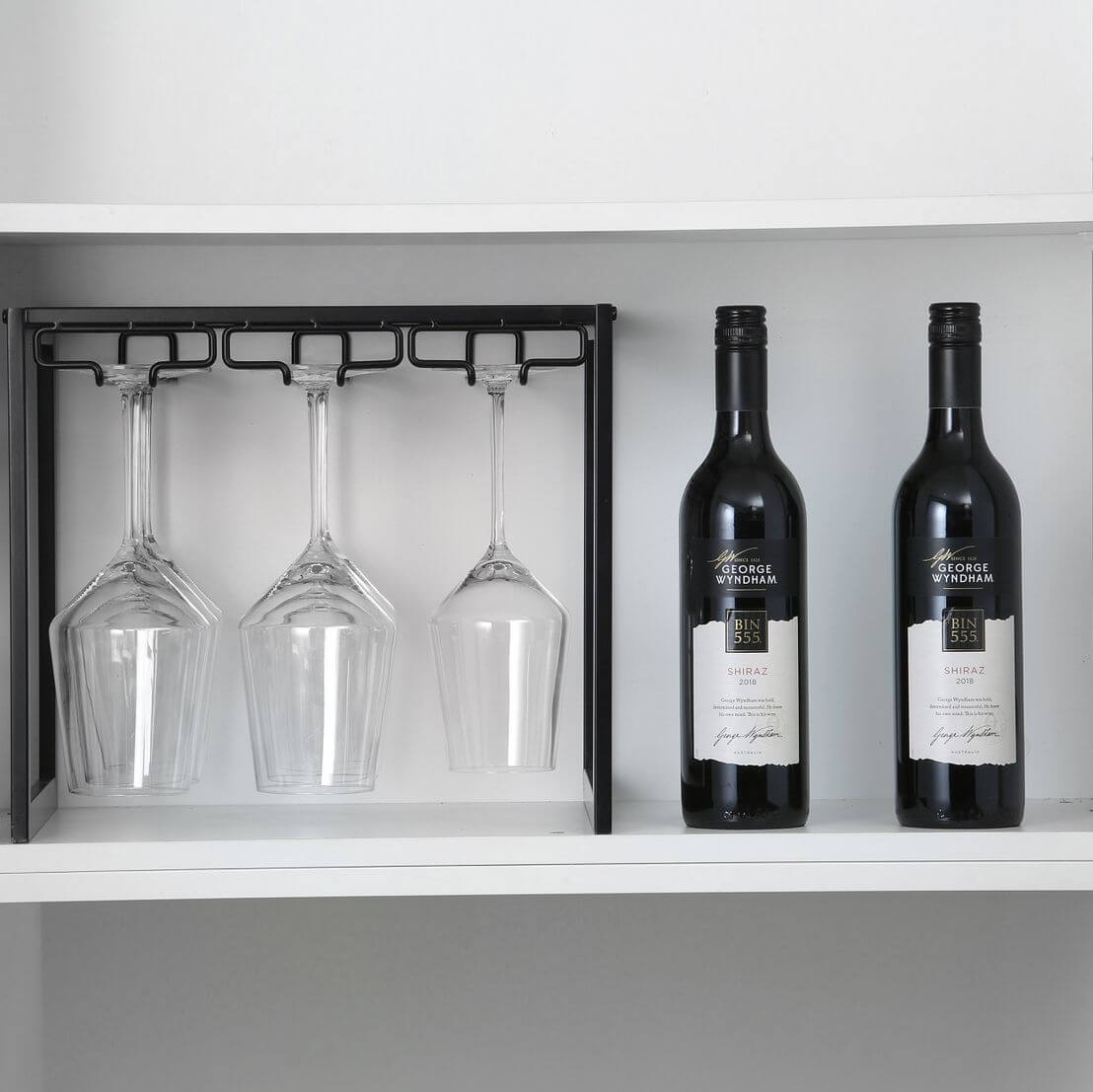 A matte black wine glass rack holding three wine glasses on a shelf