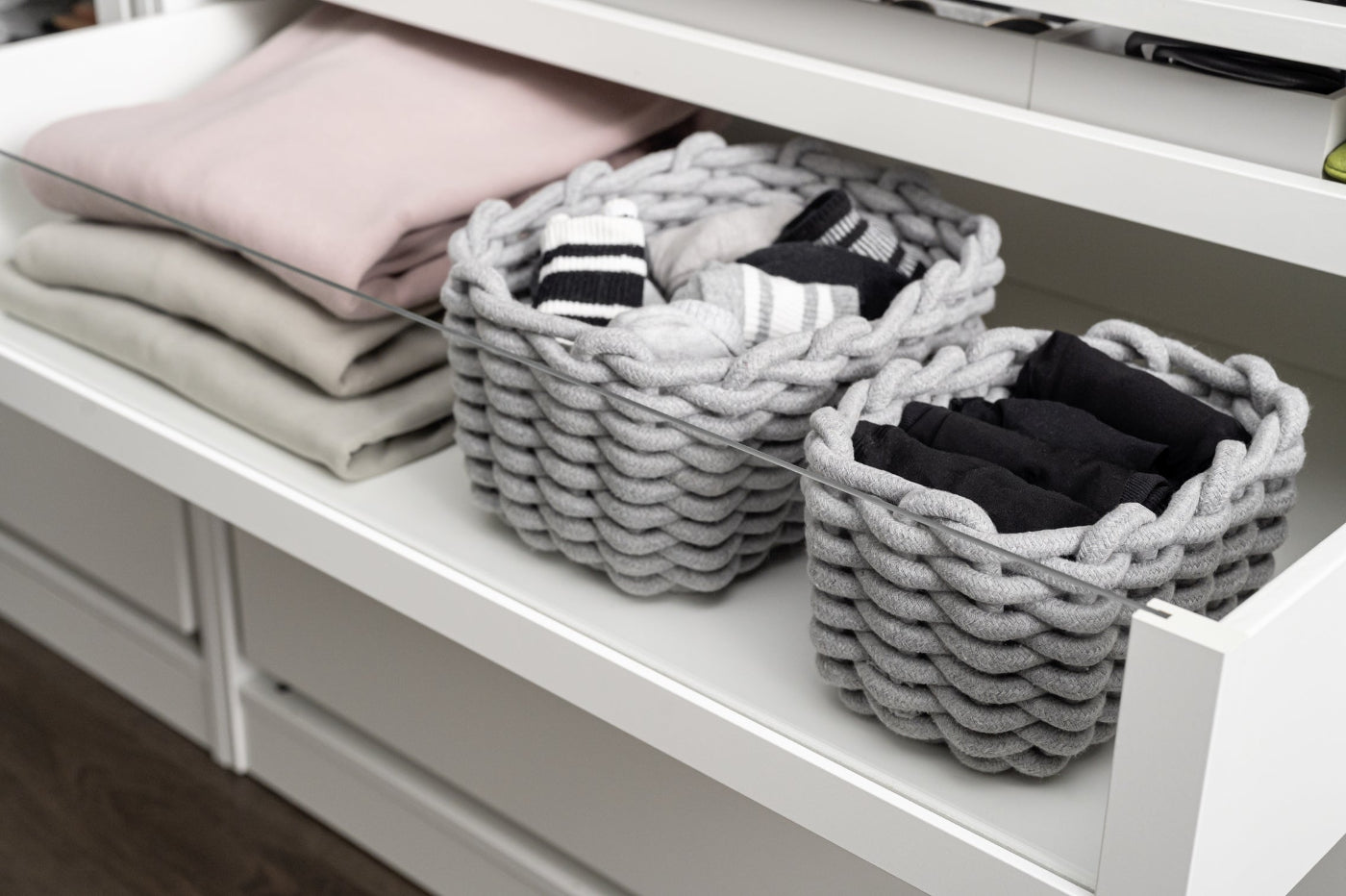 Gray woven baskets on a white shelf with folded clothes