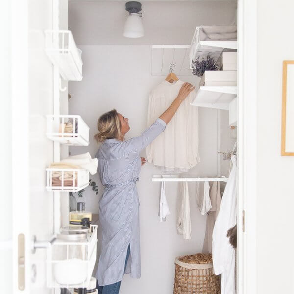 A woman hanging clothes on a White Elfa Drying Shelf in a laundry room