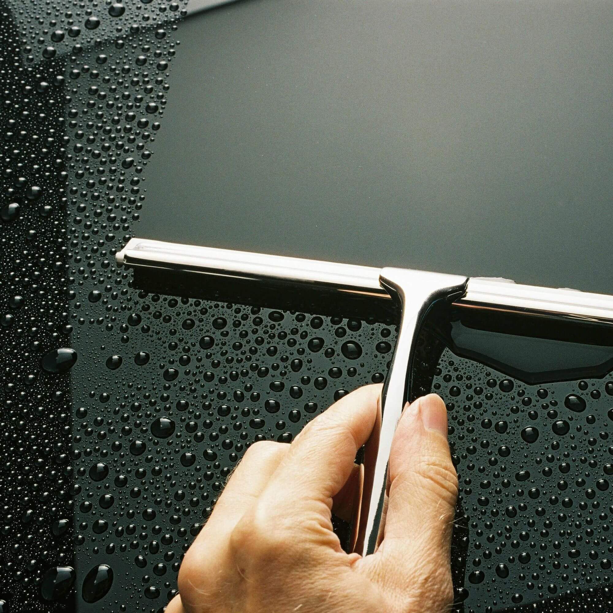 A stainless steel bathroom squeegee cleaning shower glass
