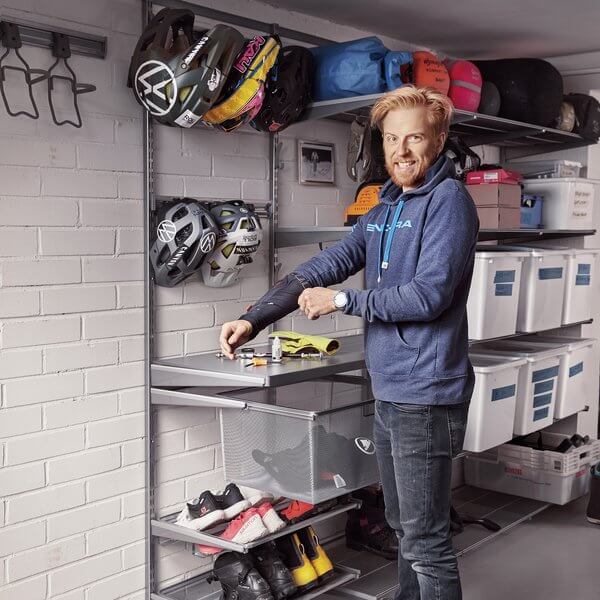 A man standing next to a Platinum Elfa garage with storage tubs and bike helmets stored
