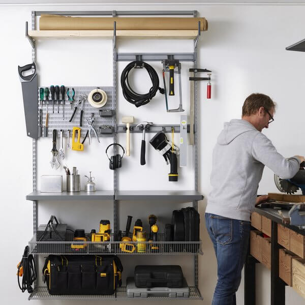 A man standing next to Platinum Elfa garage shelving with tools and power tools stored