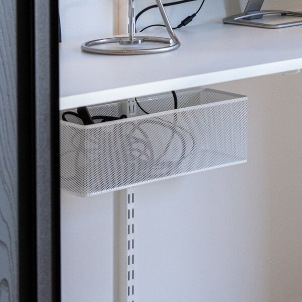 Computer cables organised under a desk with a White Elfa Mesh Utility Basket