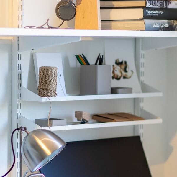 Pens, notepads and stationery organised above an office desk with two White Elfa Reversible Metal Shelf Trays