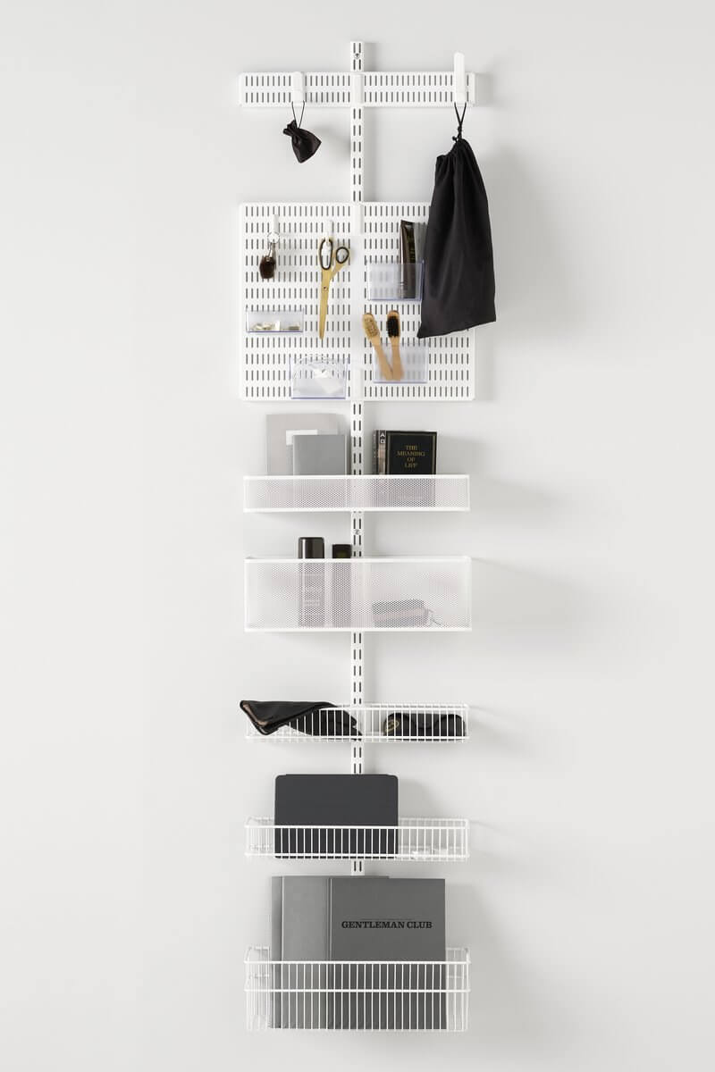 A White Elfa Utility Wall & Door system with Mesh and Wire Utility Baskets and a Centre Storing Board, used for wall-mounted storage of books, bags and stationery