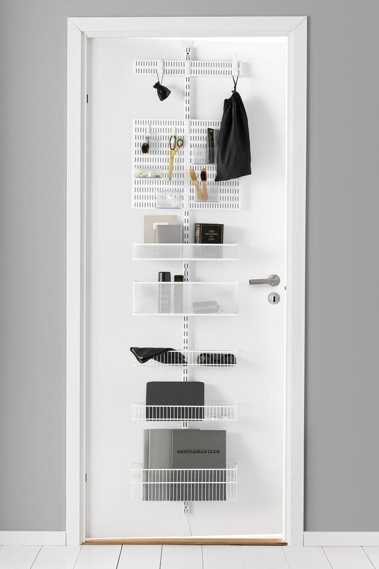 A White Elfa Utility Wall & Door system with Mesh and Wire Utility Baskets and a Centre Storing Board, used for over-the-door storage of books, bags and stationery